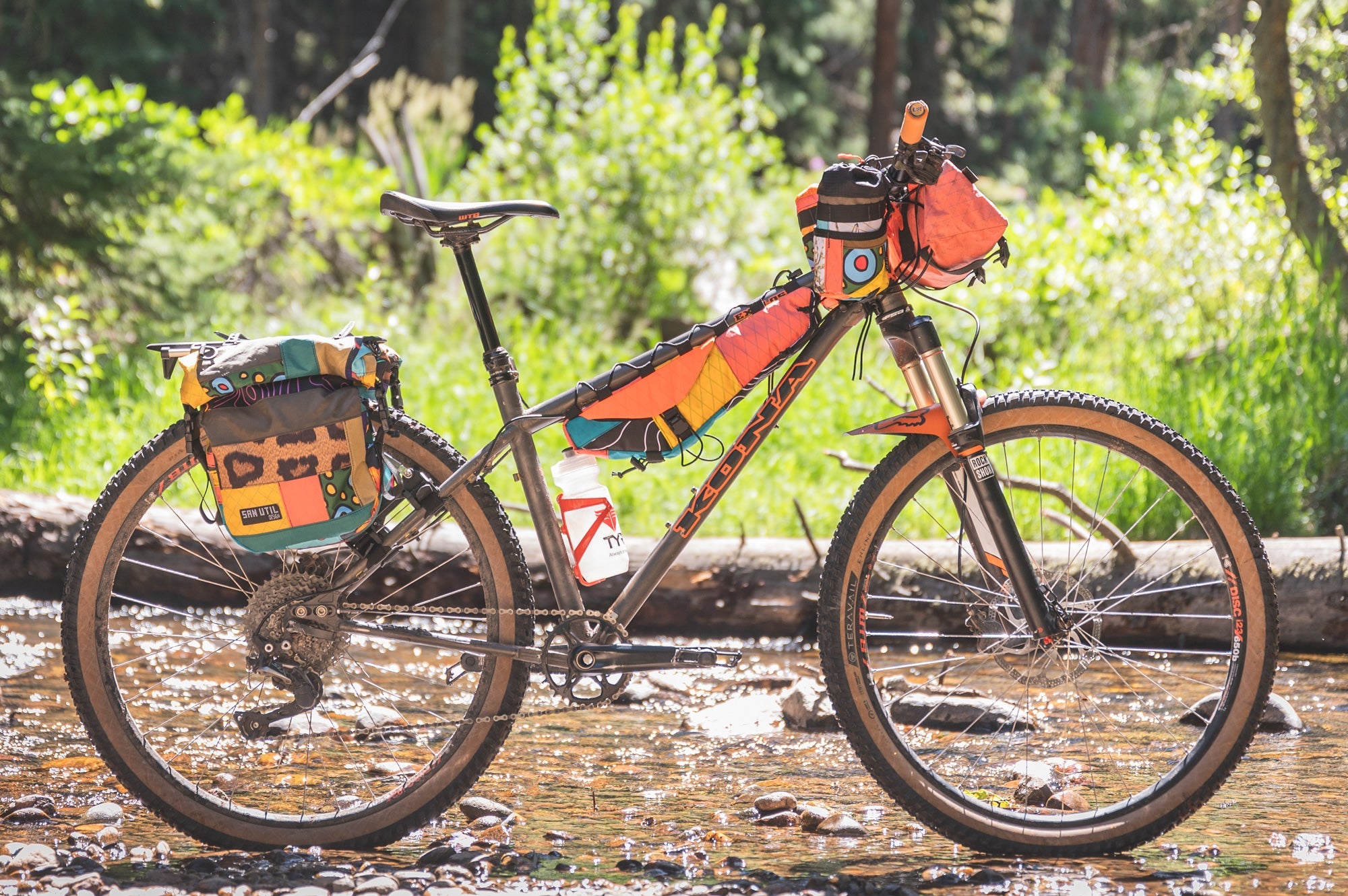 Kona Explosif sitting in stream with colourful bags attached